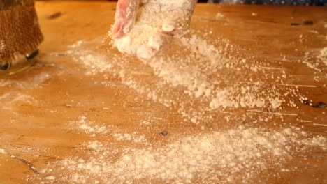 hand sprinkling flour over wooden table