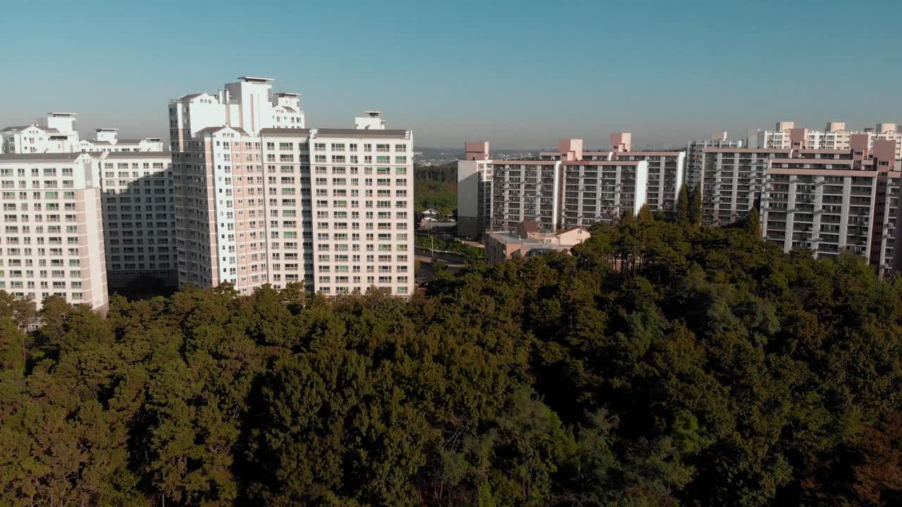 Fly in shot above trees and towards apartments