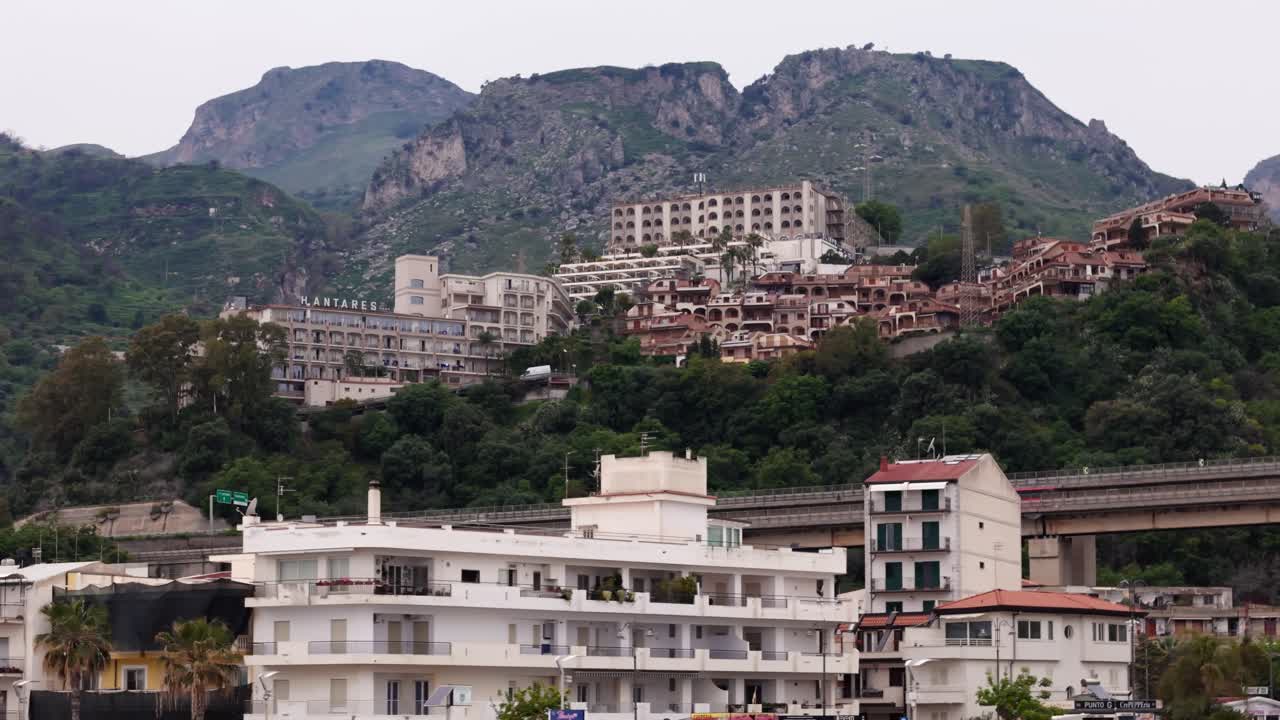 Aerial drone panning right shot showcasing buildings, an avenue, and a hidden city surrounded by nature in Letojanni, Sicily, Italy (Sicilia, Italia)