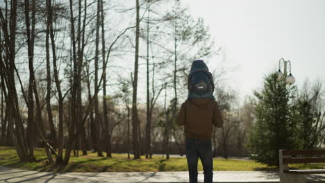 close-up of a father carrying his son on his shoulders. as he walks slowly toward the woods both are wearing a jacket and jeans trouser