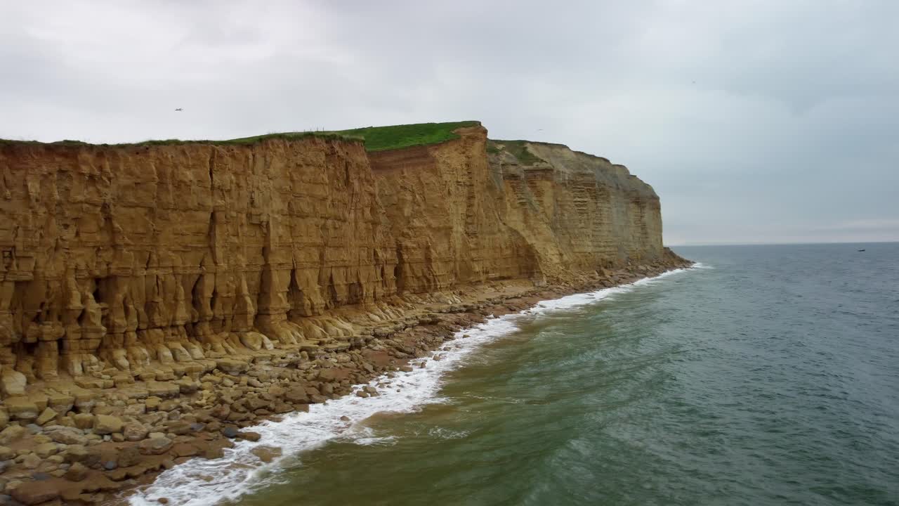 Aerial footage rotating around a Jurssaic Coast cliff in Dorset. Footage starts over the beach and then moves out to the ocean whilst rotating to the left to reveal the dramatic cliff face.