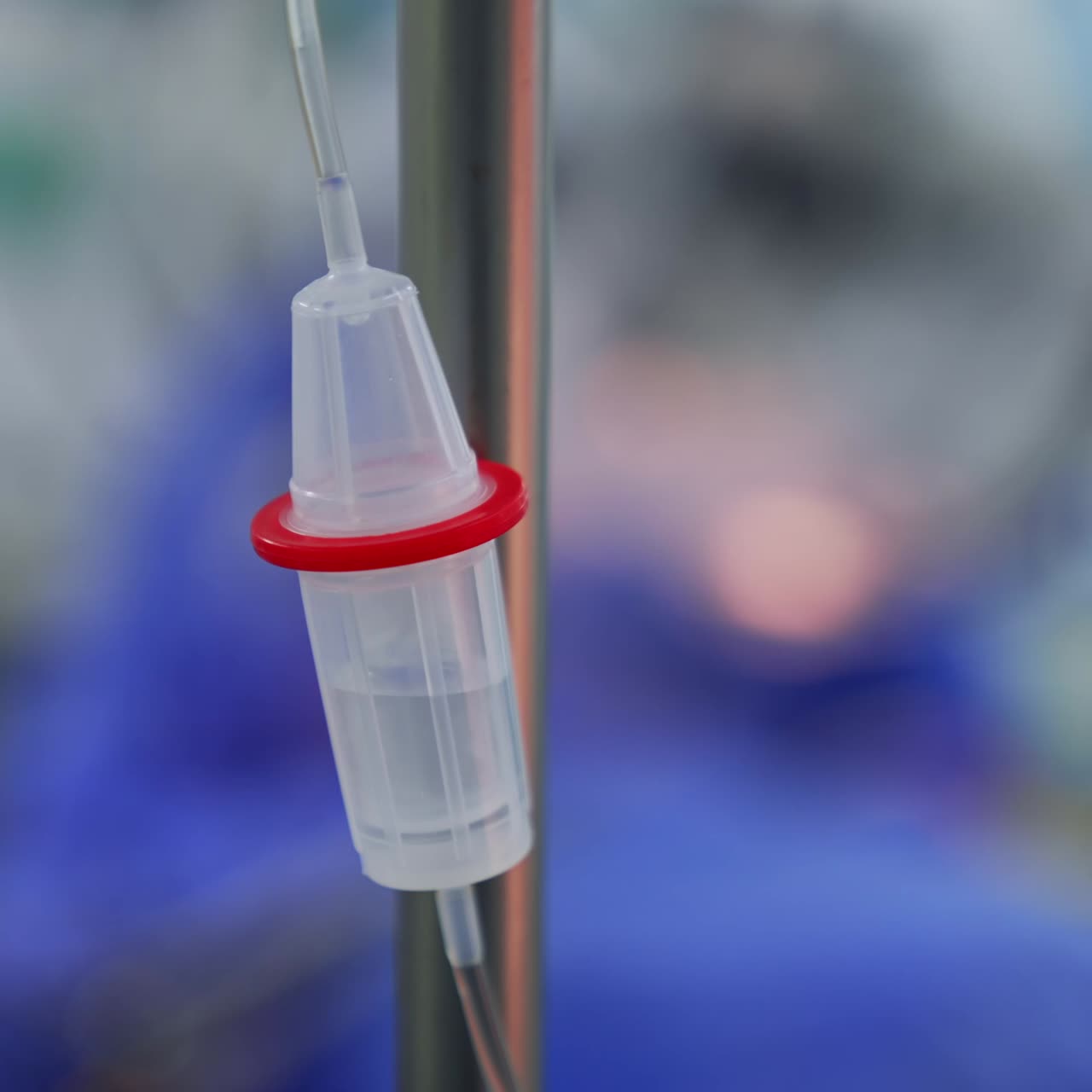 Plastic reservoir of a drop counter filled with medicines. Liquid dripping inside the dropper at surgery. Close up. Blurred backdrop