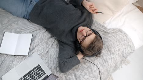 young adult relaxing on bed with headphones and laptop