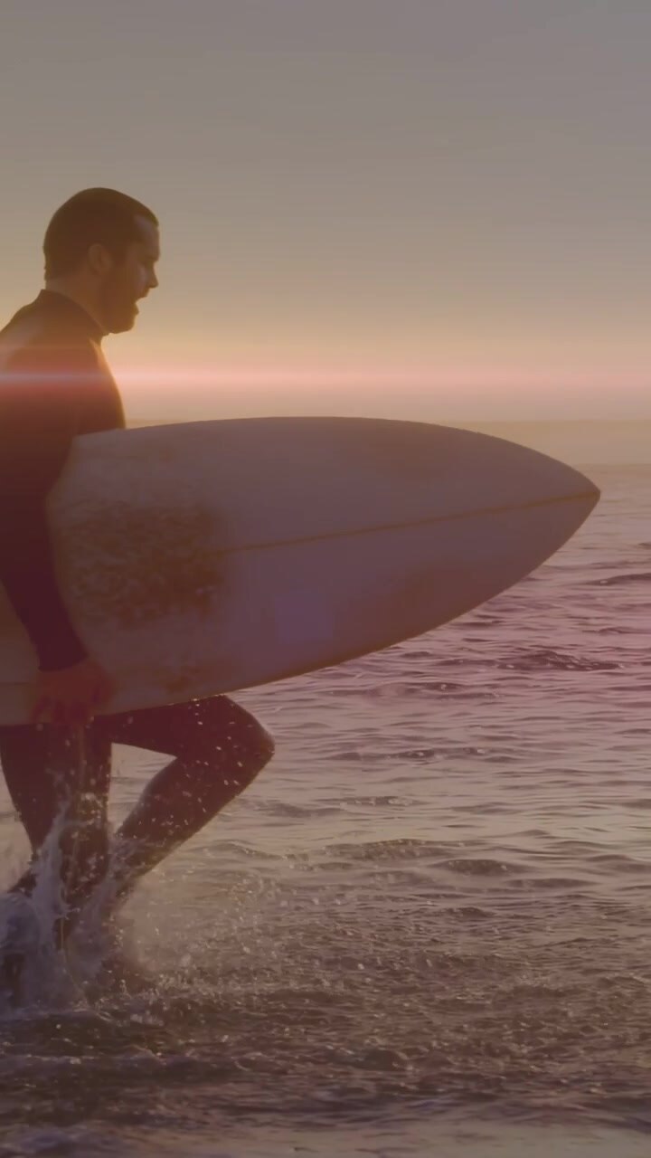 Vertical video: Board entering, surfer walking shore with board post-surf, motion splashes sports