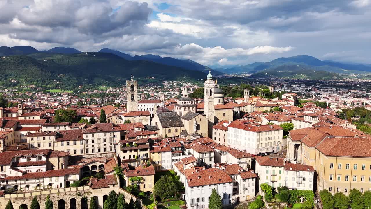 Vista aerea di Bergamo, in Italia, con tetti in terracotta, torri storiche, strutture della cattedrale e colline circostanti sotto nuvole dinamiche, con la città che si estende verso le catene montuose in lontananza