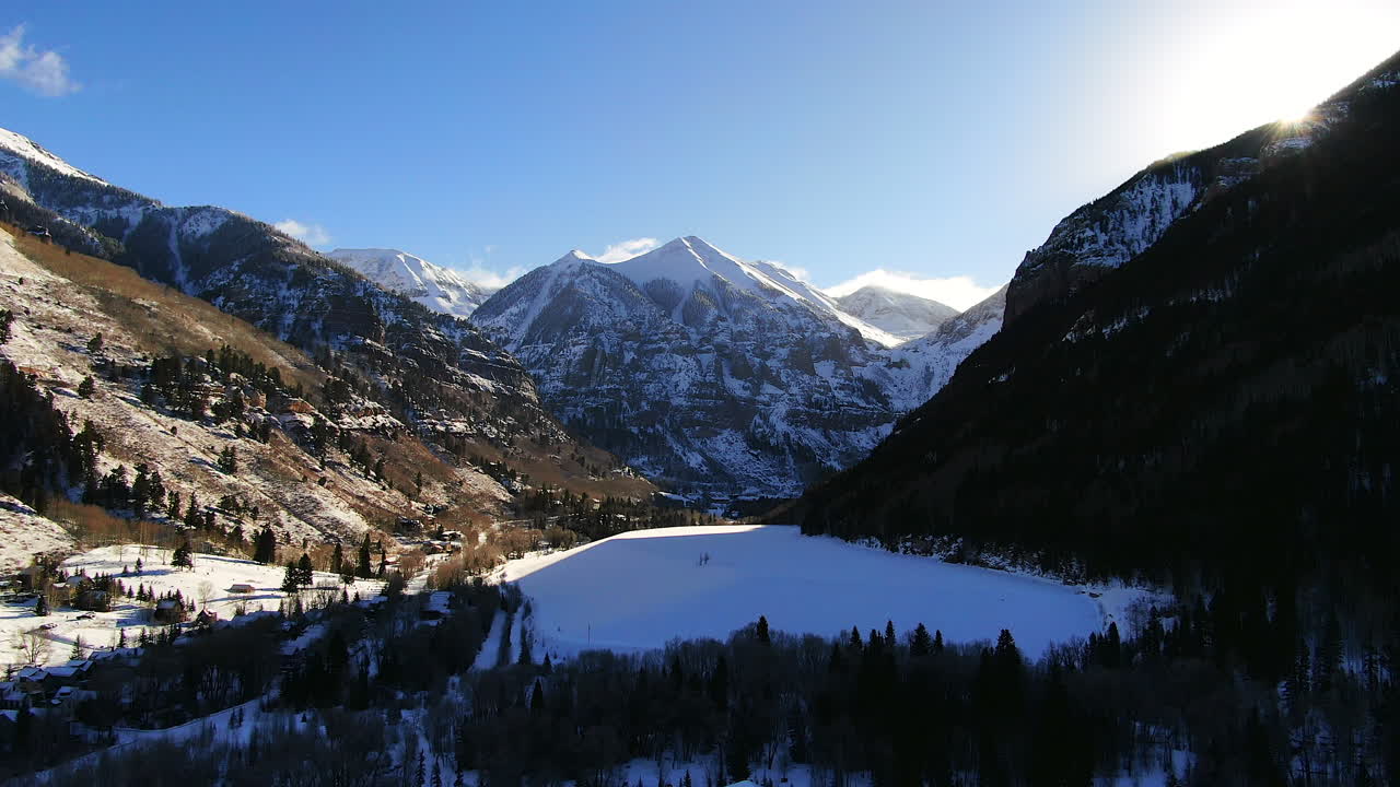 vista aérea cinematográfica de drones de la estación de esquí de montaña telluride en el centro de colorado de pintorescas montañas paisaje, lago y edificios históricos luz del sol temprano mediados del invierno movimiento hacia abajo