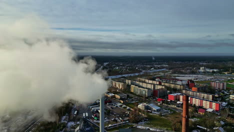 Aerial view passing a smoking factory chimney with condos in the background