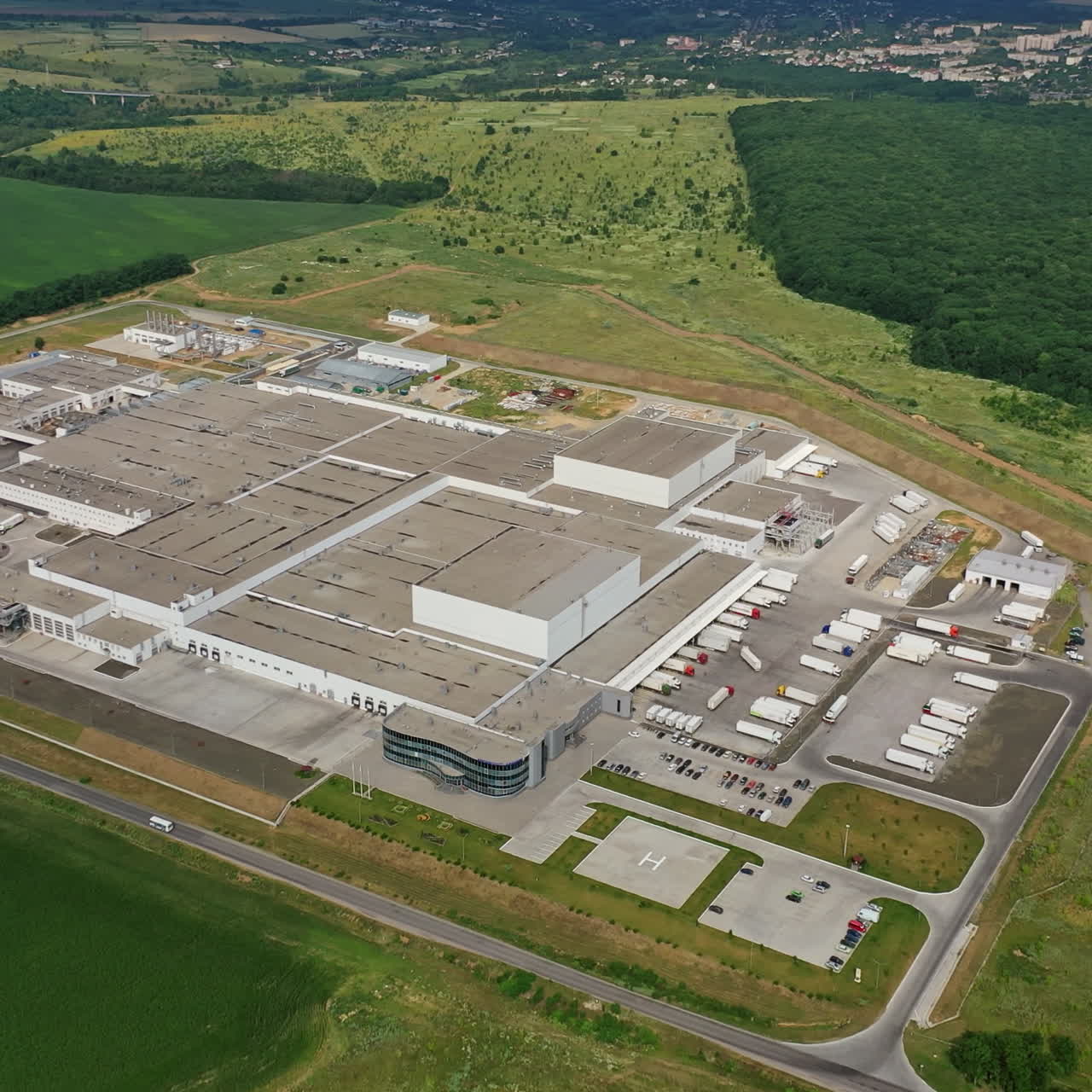 Aerial view to modern factory in the countryside. Large industrial area among green fields. Manufacturing complex outdoors.