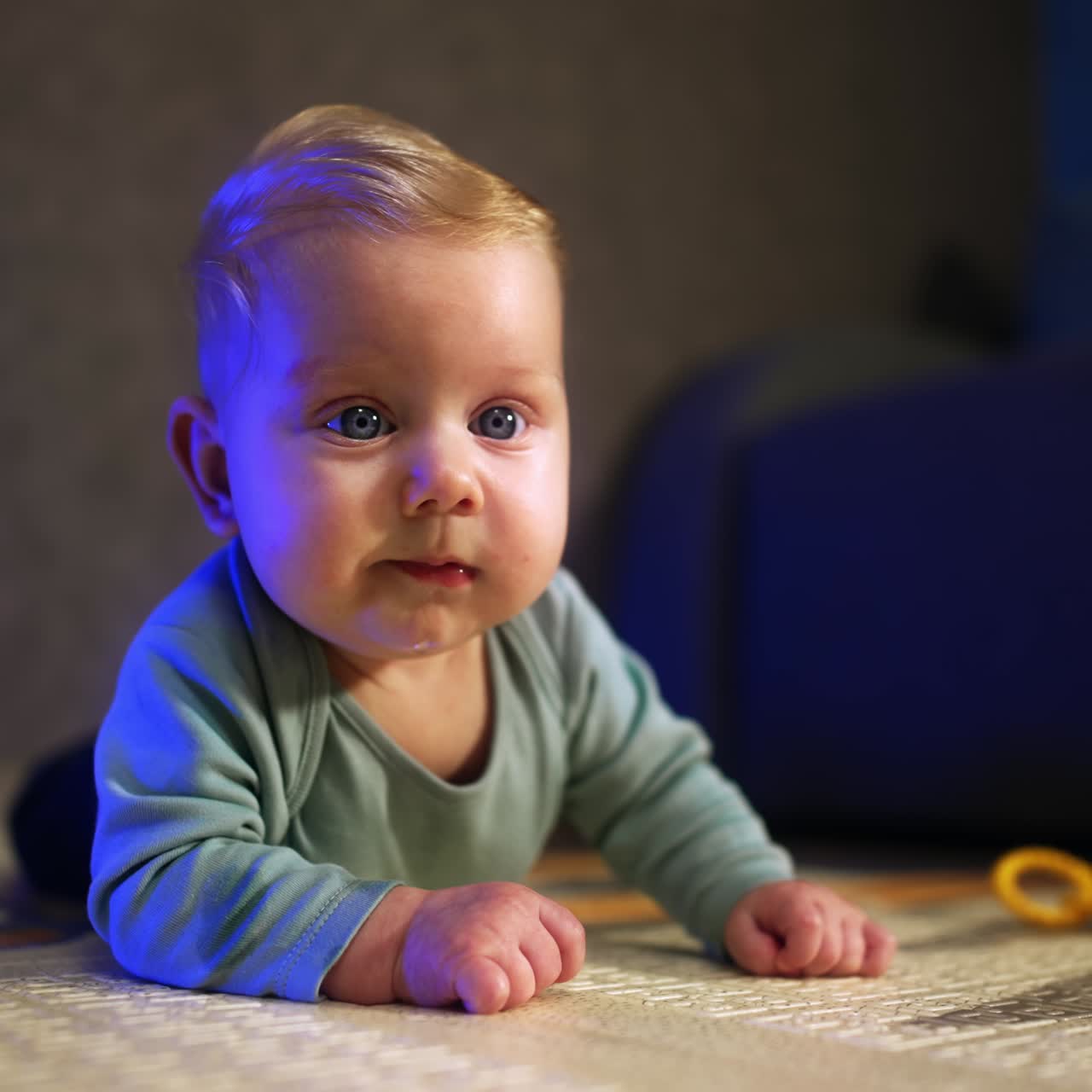 Søt, liten baby som ser seg rundt med overraskelse. Herlig barn ligger på magen foran kameraet. Nærbilde