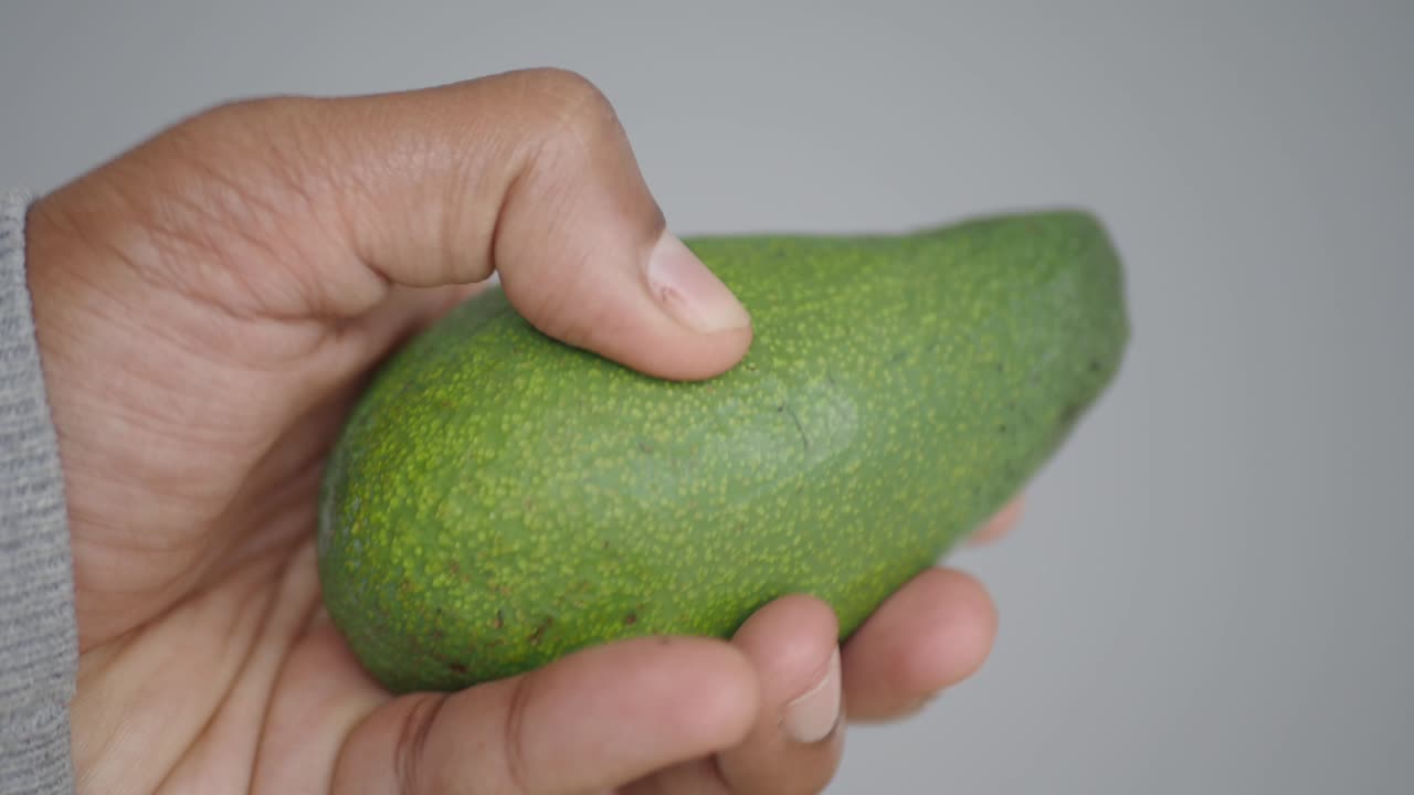 Hand holding a green avocado