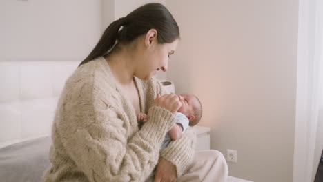 그녀의 아기를 안고 그를 애무하는 침대에 앉아 갈색 머리 여자