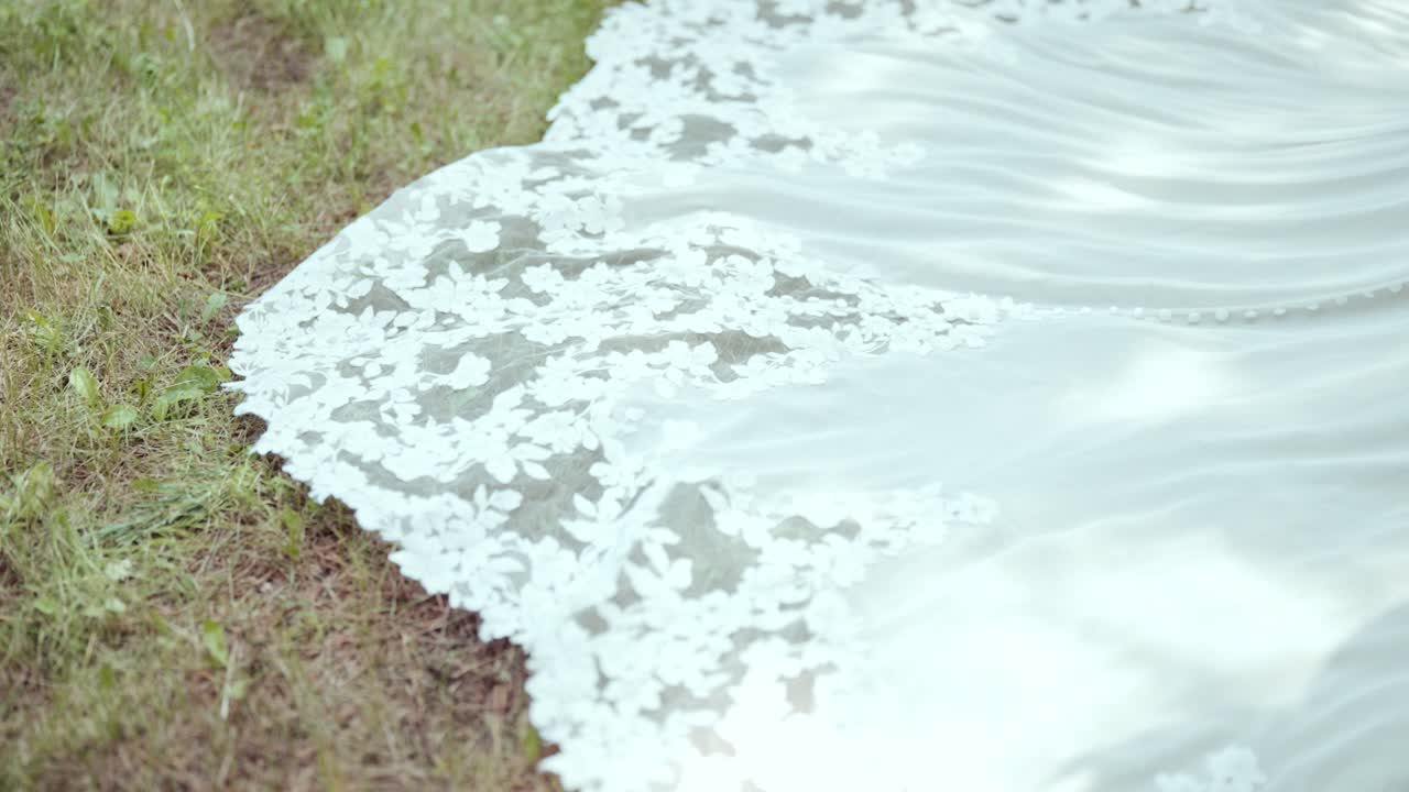 Low pan up shows ornate bridal train on grass, mesh revealing green beneath