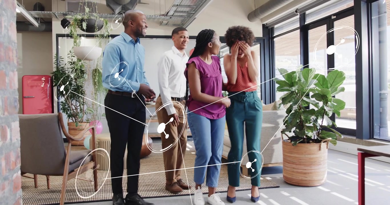 Male colleague holding smartphone, sharing tech news and sparking coworkers hugging and dancing