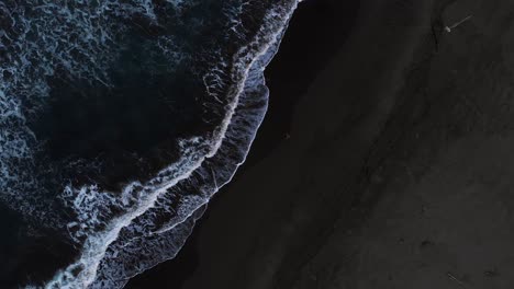 a man running on the sand at the coast in costa rica with foamy waves splashing - aerial shot