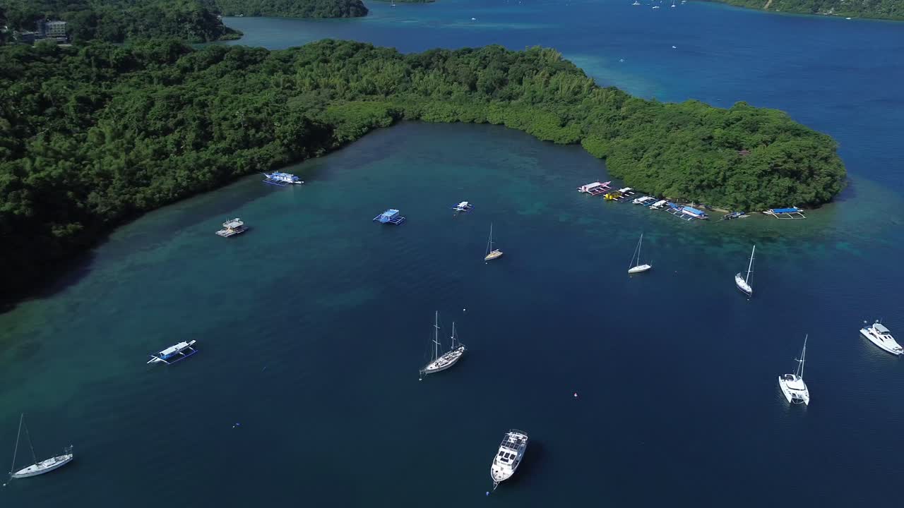 Filmato aereo realizzato con drone di piccole imbarcazioni ancorate in una tranquilla baia tropicale a Puerto Galera, nelle Filippine, circondata da una fitta foresta verde e da acque cristalline turchesi, che creano una scena di viaggio e natura rilassante