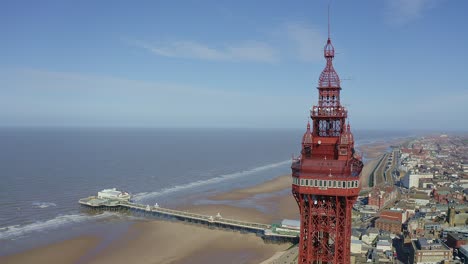 Aerial-footage,-drone-view-,-of-the-famous-Blackpool-Tower-and-beach-from-the-sky-on-a-beautiful-Summers-day-on-one-of-Great-Britains-most-popular-holiday-destinations,-tourist-attractions-by-the-sea