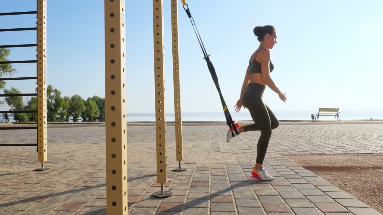 entrenamiento al aire libre. correas de suspensión. entrenamiento con correas. mujer joven atlética está haciendo ejercicios de resistencia de todo el cuerpo usando cuerdas en bucle trx, en la playa durante la puesta o el amanecer. entrenamiento de fitness al aire abierto. concepto de estilo de vida saludable. deporte matutino
