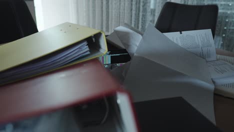 a smartphone running ai code is barely visible under messy documents and binders—symbolizing the silent presence of artificial intelligence in chaotic office or study environments