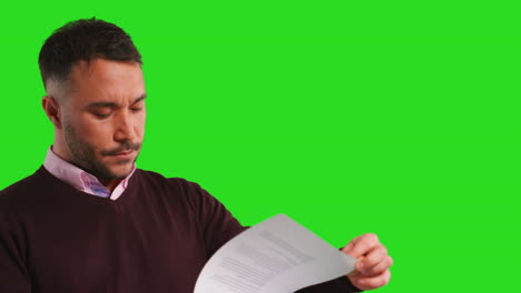 close up studio shot of male teacher or businessman standing against green screen reading document