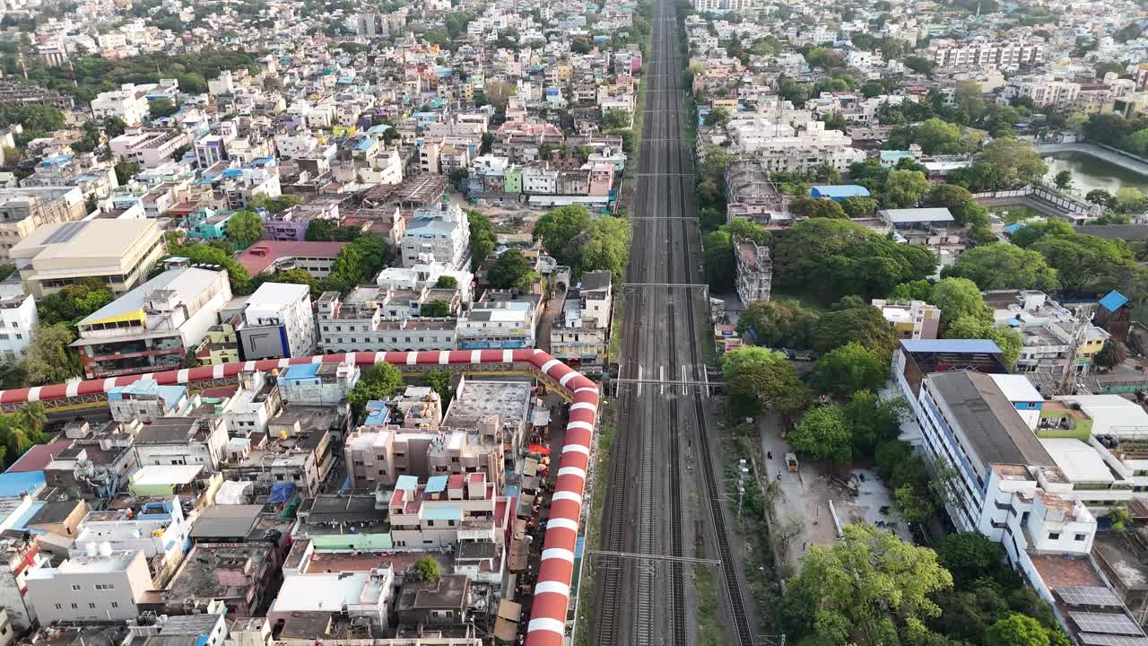A high-angle view capturing the immense scale of urban life in Chennai, Tamil Nadu. A multi-track railway line runs parallel to the elevated Mass Rapid Transit System (MRTS) tracks,