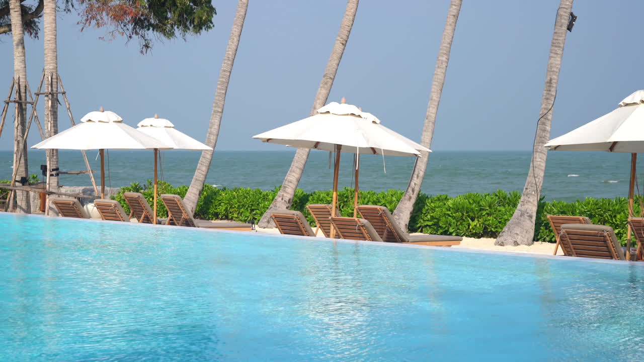 바다를 배경으로 수영장 주변에 침대 수영장이 있는 우산 - 휴일 및 휴가 개념