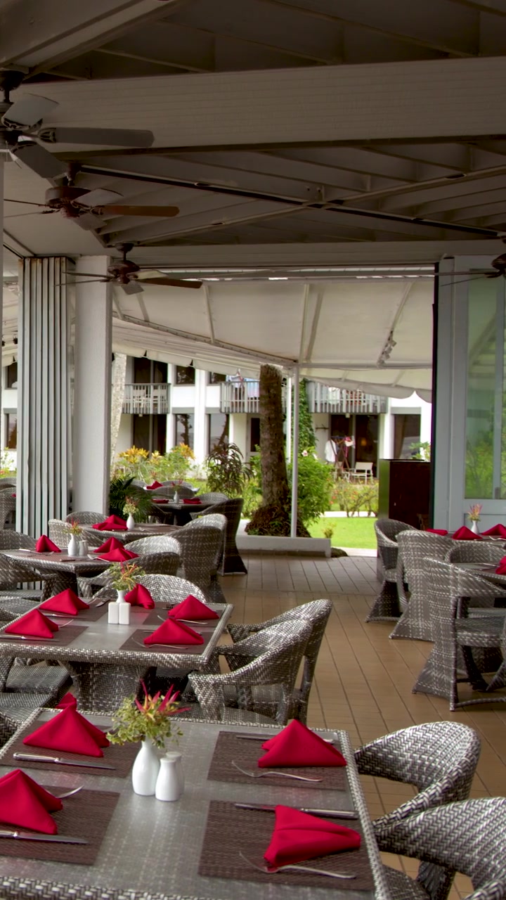 Un plano panorámico lento revela una zona de comedor exterior de lujo vacía en un resort tropical.
