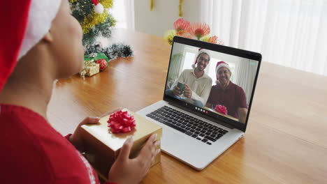 Mujer-Afroamericana-Con-Gorro-De-Papá-Noel-Usando-Una-Computadora-Portátil-Para-Una-Videollamada-Navideña,-Con-La-Familia-En-La-Pantalla