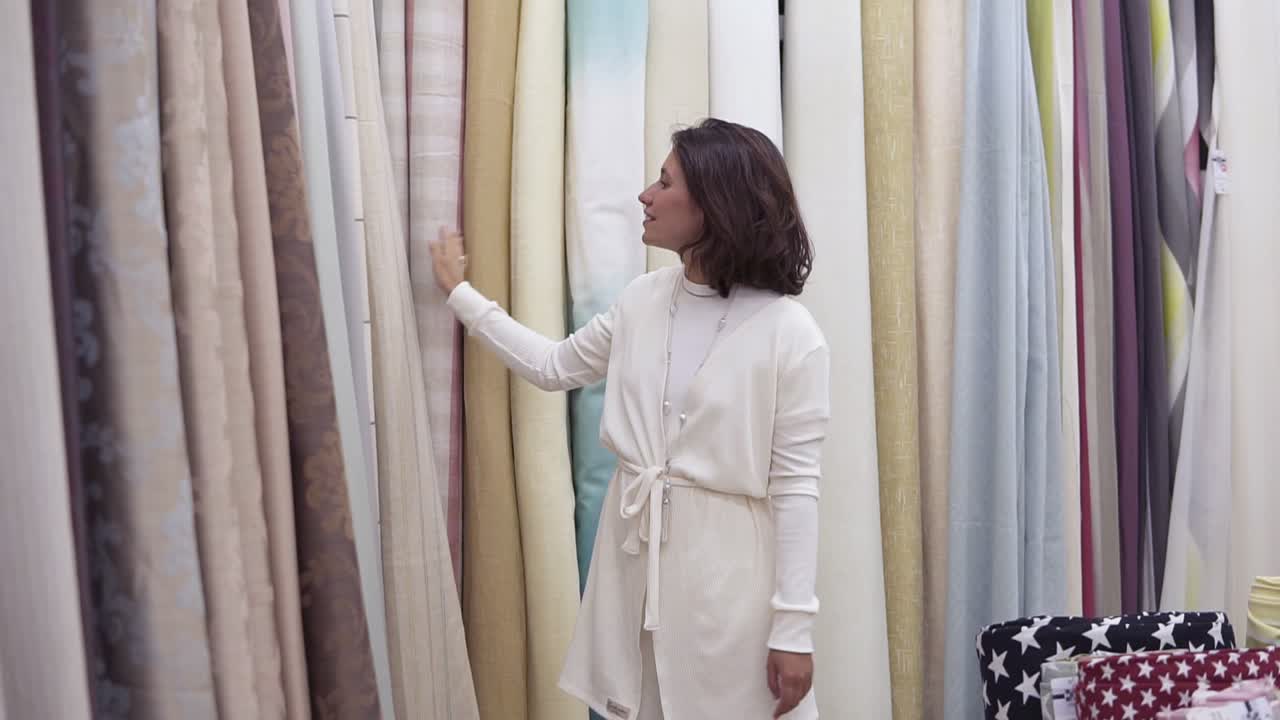 una hermosa mujer joven entre la gran variedad de telas en la tienda. ella sonríe, mira a su alrededor, pasando una mano tocando la textura. variedad de colores. cámara lenta