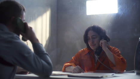 inmate discussing case with officer through glass in prison interrogation room