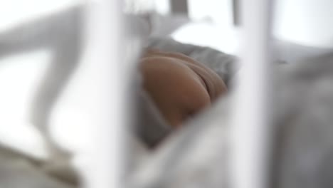 close view through white swinging white crib of cute sleeping baby