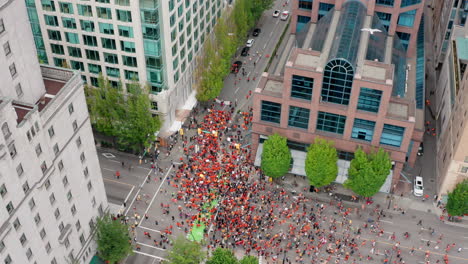 huge crowd of protesters march below, rising tilt down aerial reveal in uhd