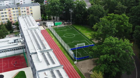 Aerial-reveal-shot-of-a-school-football-field-with-artificial-grass-and-a-big-coal-mine-in-the-background,-4K-drone