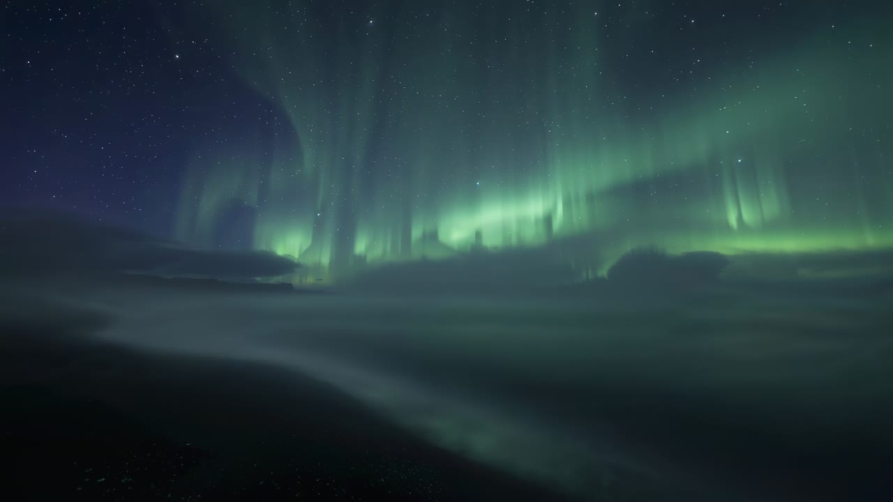 Unfolding aurora forming green curtain bands over polar coast after solar wind, reflecting on water