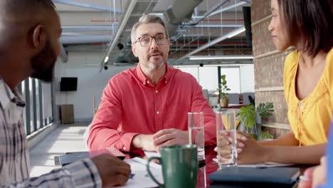 Team-of-diverse-colleagues-discussing-while-sitting-on-a-table-together-at-office