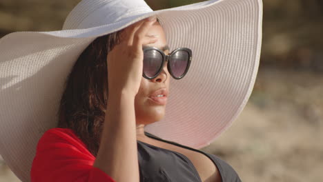 portrait shot of latin girl model wearing sunhat and sunglasses on beach holiday smiles, closeup