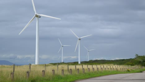 wind turbines with low pan across road to fence and yellow grass field