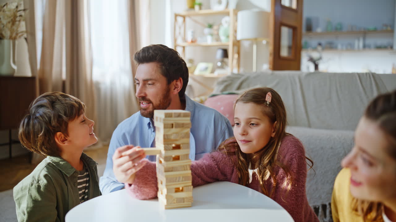 Famiglia che costruisce una torre di legno e trascorre il fine settimana seduta sul tappeto in un appartamento, primo piano