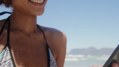 vista frontal de una joven mujer afroamericana en bikini usando teléfono móvil en la playa 4k