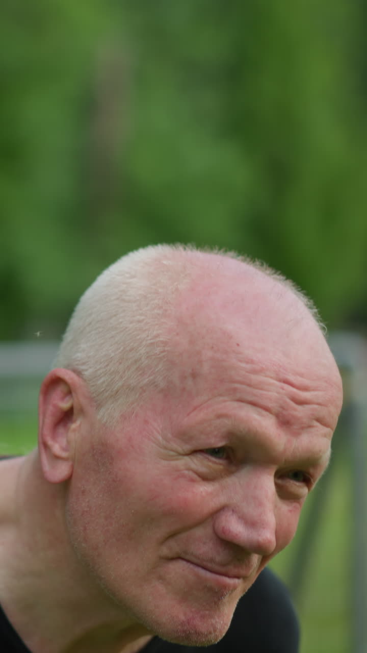 한 노인이 숙련된 방법으로 축구공을 멀리 이끌고, 그의 얼굴은 집중되고 결단력있으며, 골 포스트와 잔디을 흐릿하게 볼 수 있습니다.