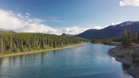 Sensational-low-fast-flight-above-Yukon-Takhini-river-waters-in-rural-countryside-with-picturesque-landscape-and-mountain-range-in-background-on-sunny-day,-Canada,-overhead-descend-drone