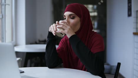 Attractive-female-with-unbelievably-beautiful-eyes-and-hijab-is-drinking-cappuccino.-Indoors-footage