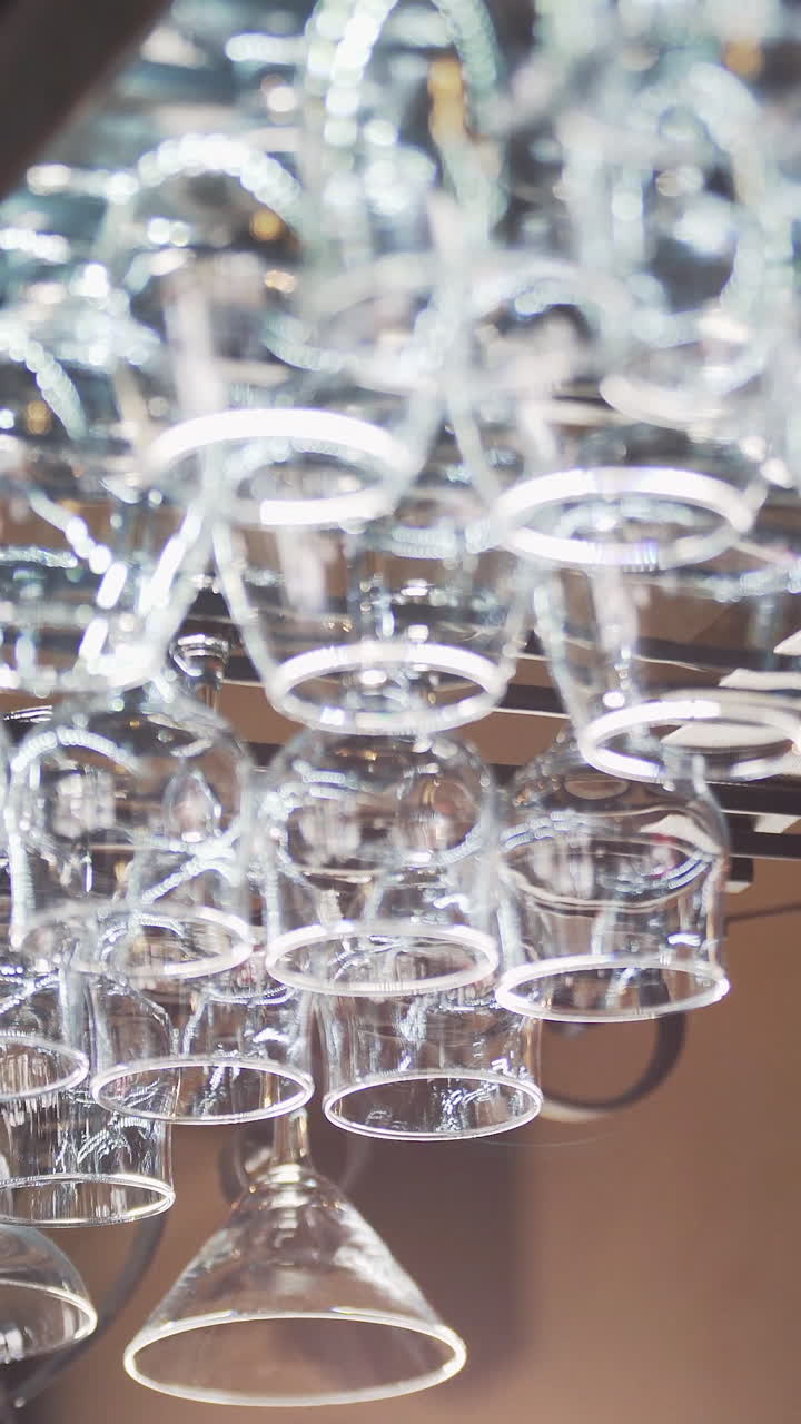 Different glasses hanging from a glassware holder above the bar counter. Clean glasses upside down in a bar. Vertical video.