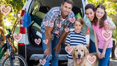 multiple pink heart icons floating against caucasian family with their pet dog on a picnic