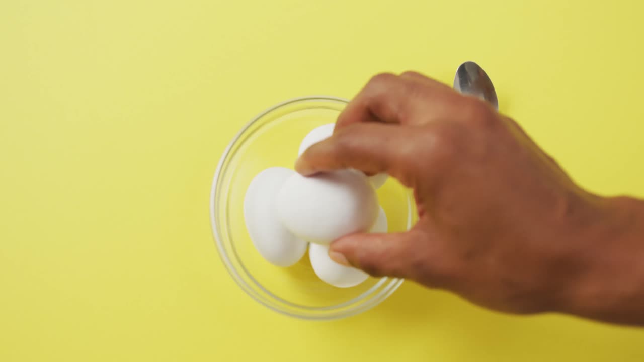 Video of close up of biracial man putting egg into bowl on yellow background
