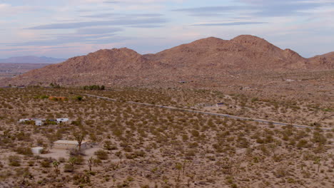 Aerial-of-desert-in-Joshua-Tree,-California-with-a-pan-right-tracking-with-a-white-truck-as-it-drives-through-the-landscape