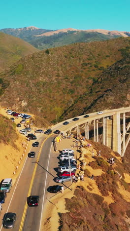 cars moving slowly to and from the bridge in the mountains. california rocks at the coast of pacific on sunny daytime. aerial view. vertical video