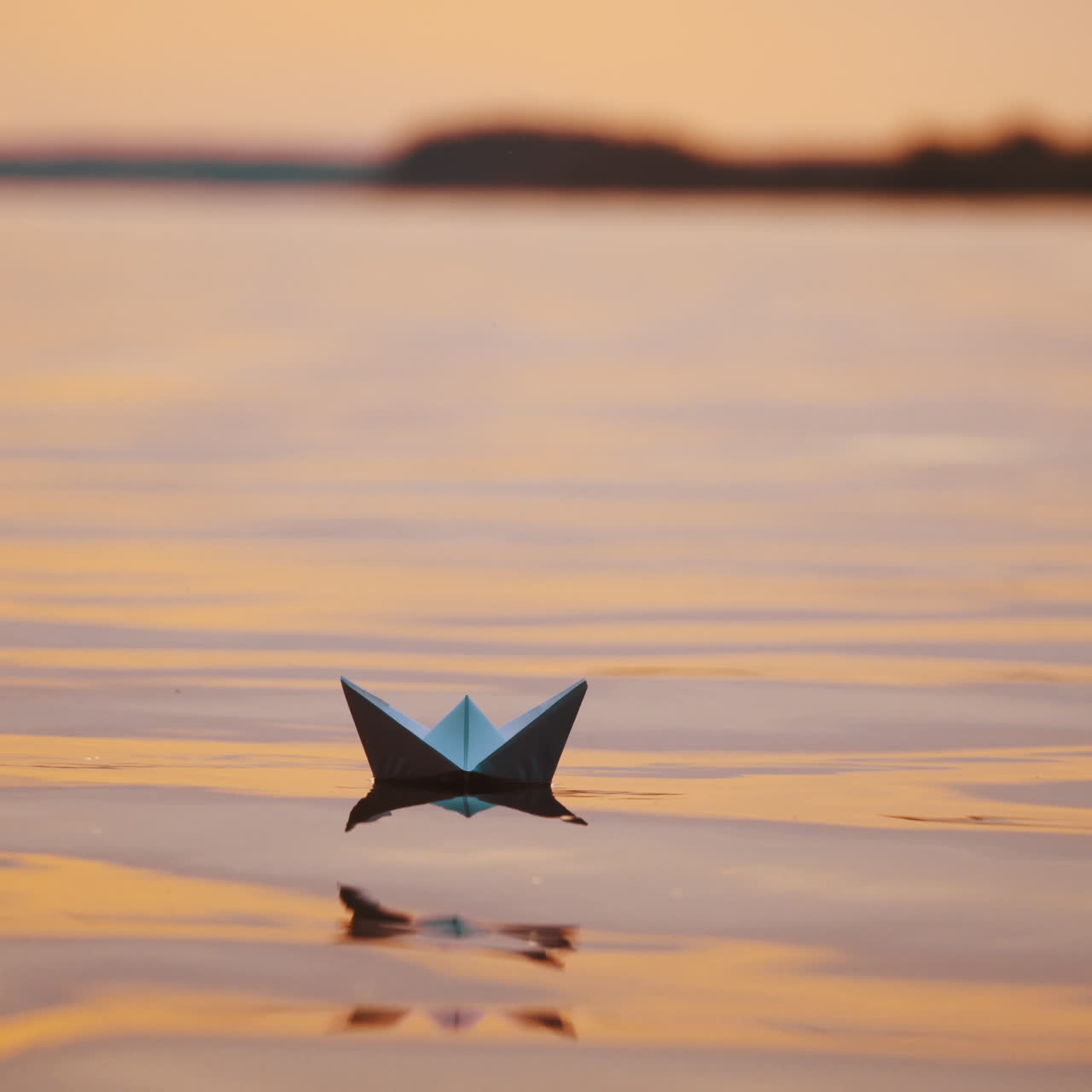 Paper ships on water surface at sunset. One origami boat floating in the river and another one joins to it.