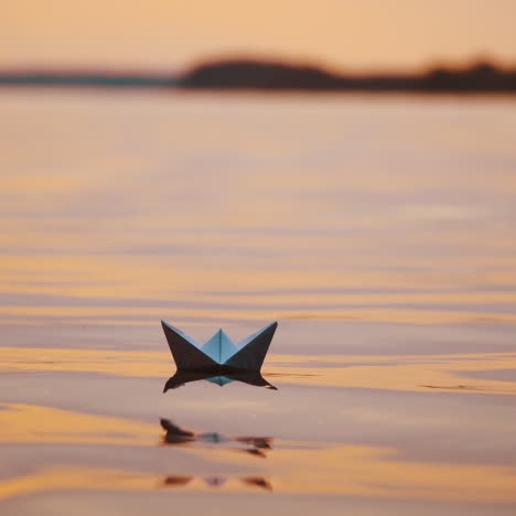 Paper ships on water surface at sunset. One origami boat floating in the river and another one joins to it.