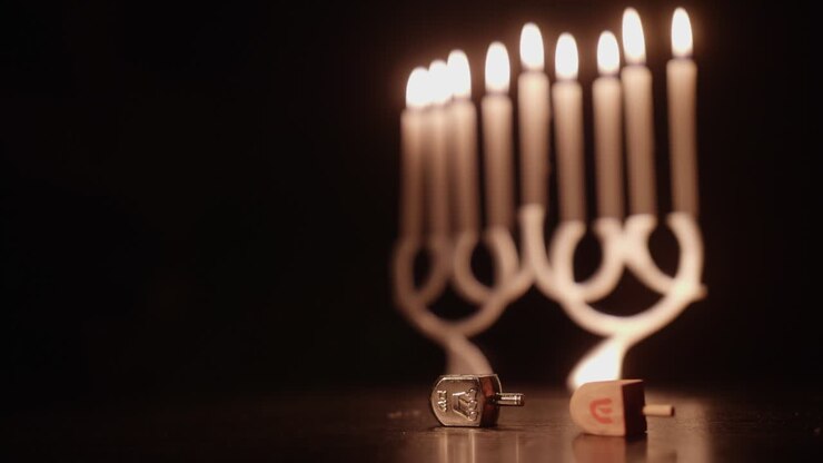 Hand Spinning a Dreidel with a Lit Menorah in the Background