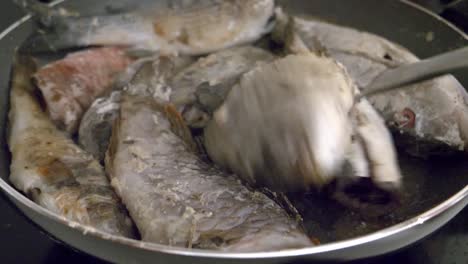 la mujer fríe y gira el pescado en la sartén con una vista de cerca